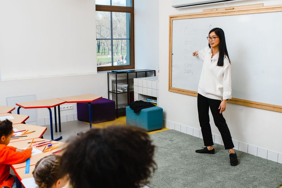 Female teacher instructing a group of diverse students in a modern classroom with natural light.