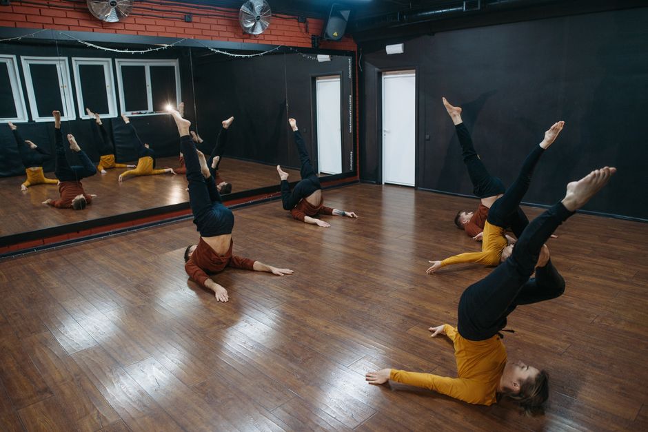 Dancers practicing dynamic moves in a modern dance studio with mirrored walls.